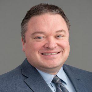 A headshot of Dr. Robert Guzy in a gray suit and tie.