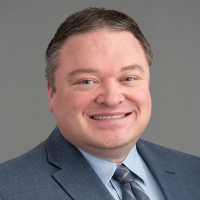 A headshot of Dr. Robert Guzy in a gray suit and tie.