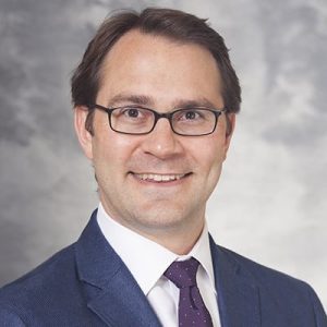 A headshot of Dr. Daniel McCarthy wearing a dark blue suit and purple tie.