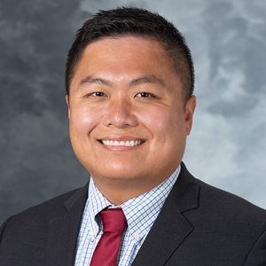 A headshot of Dr Yu Xia wearing a dark suit and red tie.