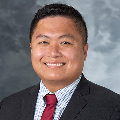 A headshot of Dr Yu Xia wearing a dark suit and red tie.